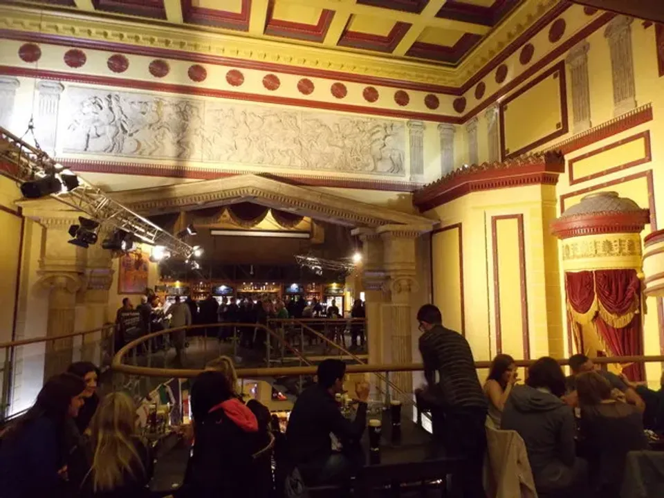 The ornate former-theatre interior of the Prince of Wales pub in Cardiff, drinkers at tables below the old stage