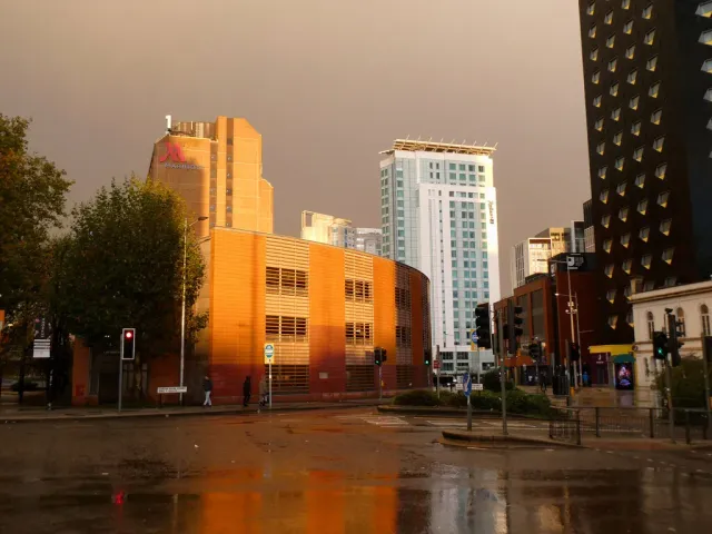 Wet Cardiff city-centre streets glowing gold at dusk after rain, with the Marriott and Radisson towers rising behind